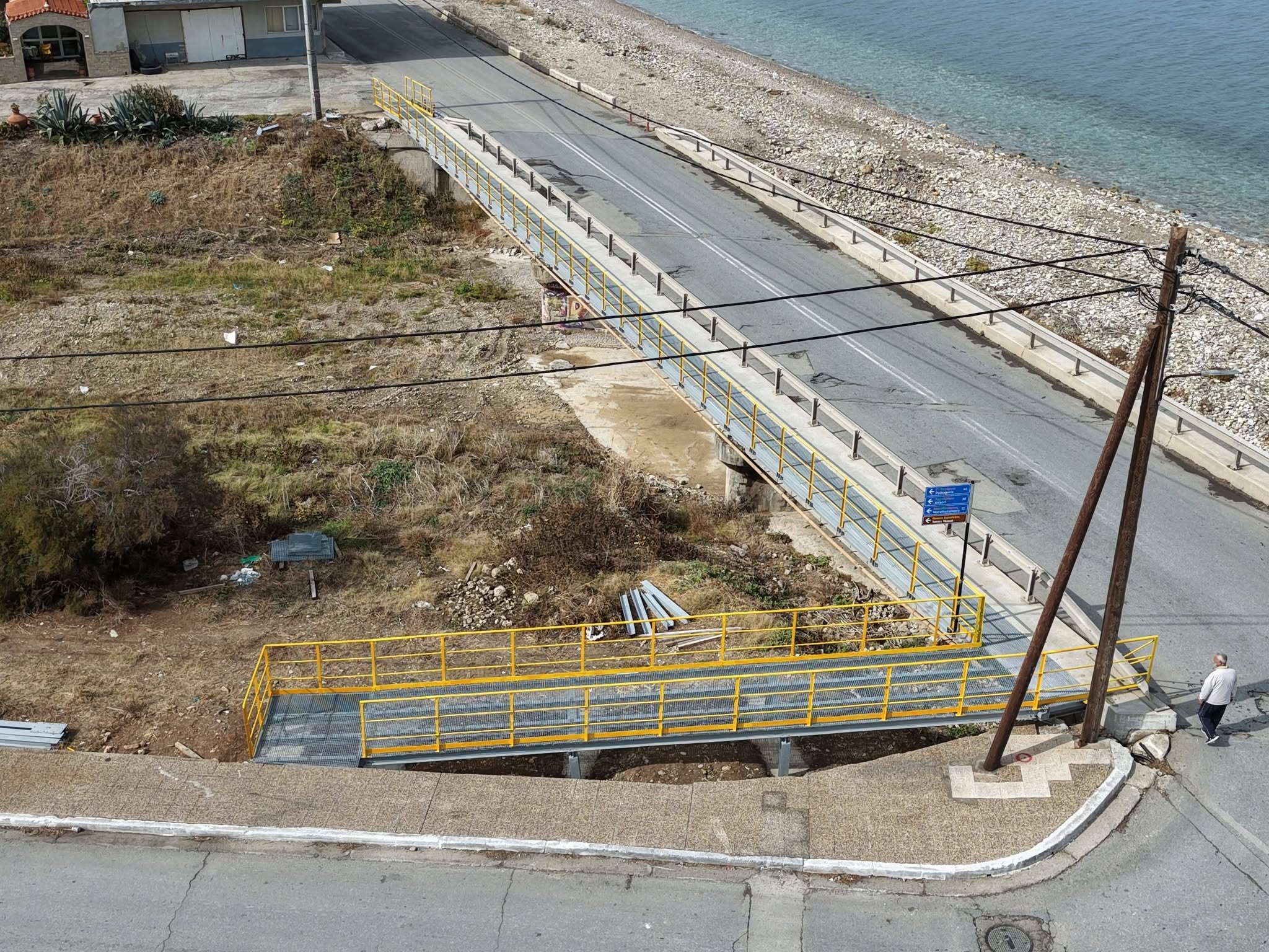 Η μεταλλική πεζογέφυρα με κίτρινα κιγκλιδώματα δίπλα στην οδική γέφυρα, στην εκβολή του Κερκήτιου ρέματος στο Καρλόβασι.