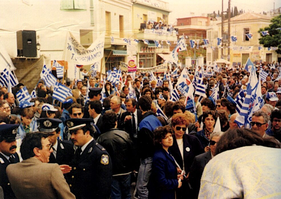 Πλήθος συγκεντρωμένων με ελληνικές σημαίες και σημαίες της Νέας Δημοκρατίας σε δρόμο της Σάμου.