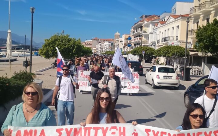 Διαδηλωτές με πανό κατά των συγχωνεύσεων σχολικών τμημάτων και σημαίες στην παραλιακή λεωφόρο Θεμιστοκλή Σοφούλη στη Σάμο.