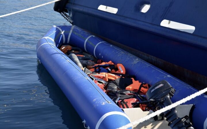 Μπλε φουσκωτό σκάφος με εξωλέμβια μηχανή και σωσίβια, δεμένο δίπλα σε μεγαλύτερο πλοίο.